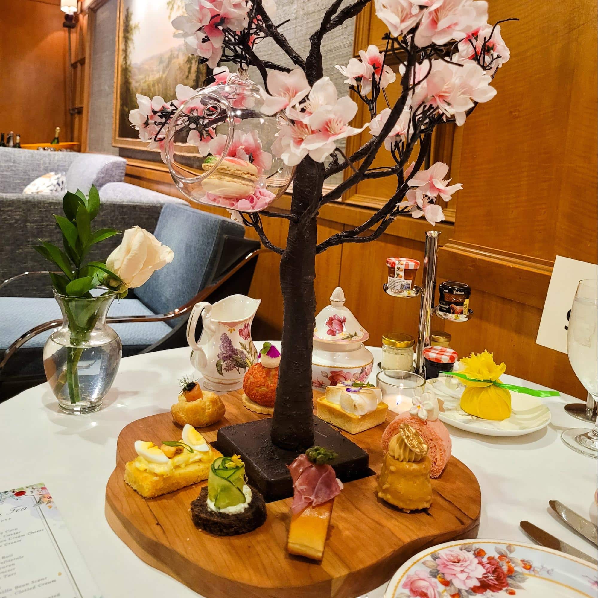 A wooden tray with assorted savory and sweet courses, centered around a cherry blossom tree centerpiece at Afternoon Spring Tea, Ritz Carlton Atlanta.