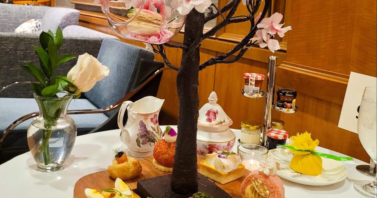 A wooden tray with assorted savory and sweet courses, centered around a cherry blossom tree centerpiece at Afternoon Spring Tea, Ritz Carlton Atlanta.