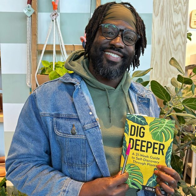 KB holding a book titled "Dig Deeper" by Alisha Bridges in front of a plant display