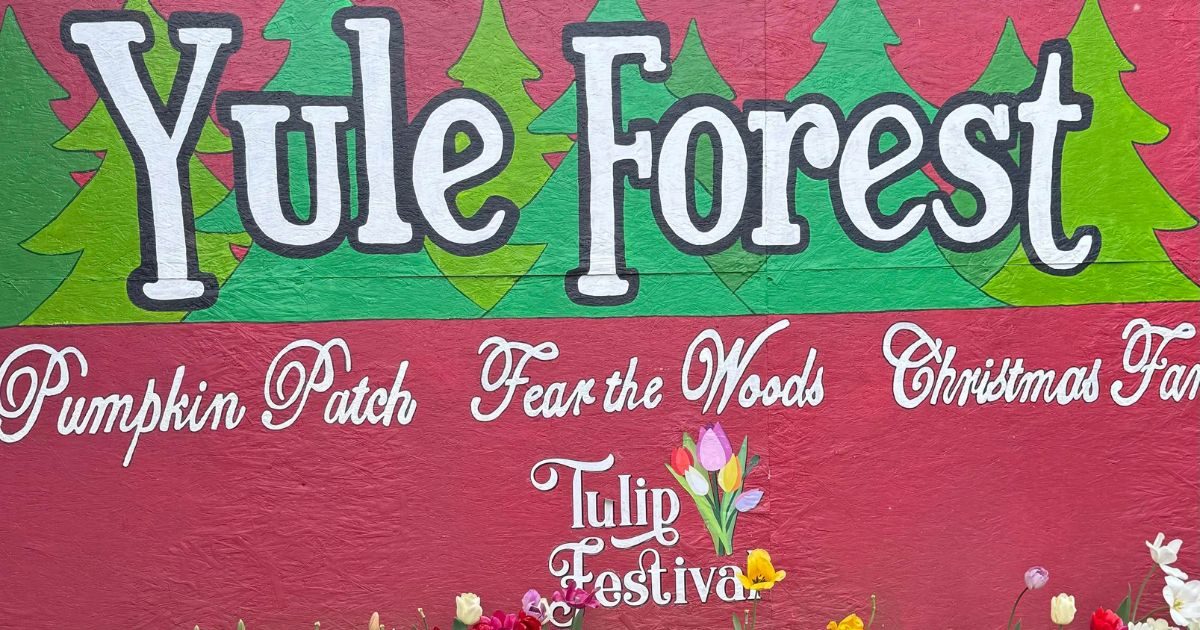 Welcome to Yule Forest sign, showcasing various seasonal events with tulips in the foreground.